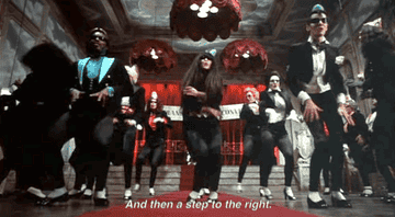 the cast dancing to &quot;And then a step to the right&quot; in a large hall with stairs