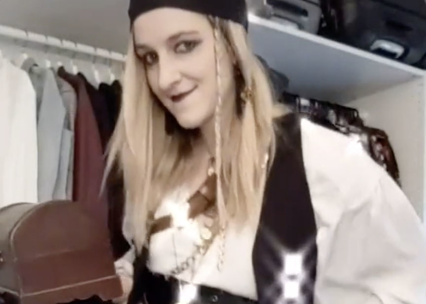 A woman wears a pirate costume with a best, lots of jewelry and a bandana on her head