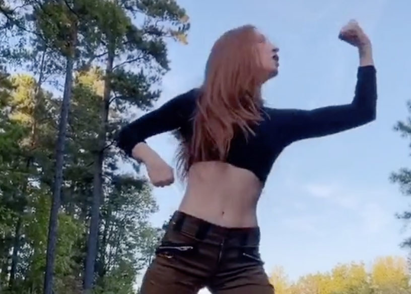 A woman flexes while wearing a black crop top and green cargo pants