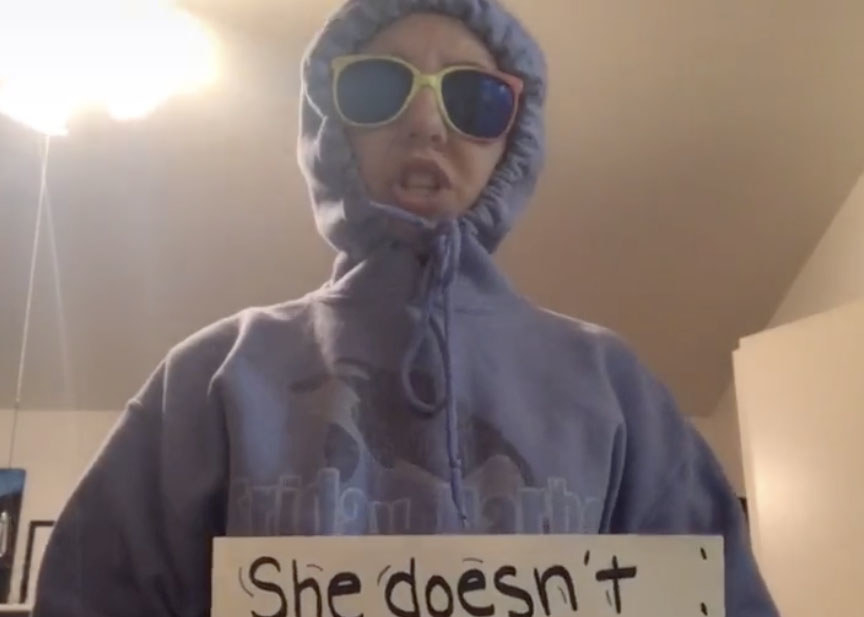 A woman wears a blue hoodie with the hood pulled tight and sunglasses