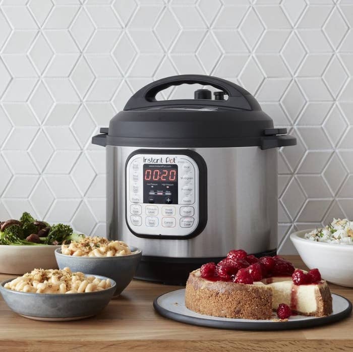Silver instant pot with black lid in back of mac n cheese, broccoli, and a cheesecake