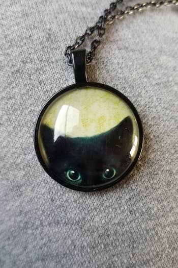 The necklace with a round pendant showing a cat's ears and eyes peeking up from the bottom