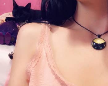 A reviewer wearing the necklace next to their own black cat