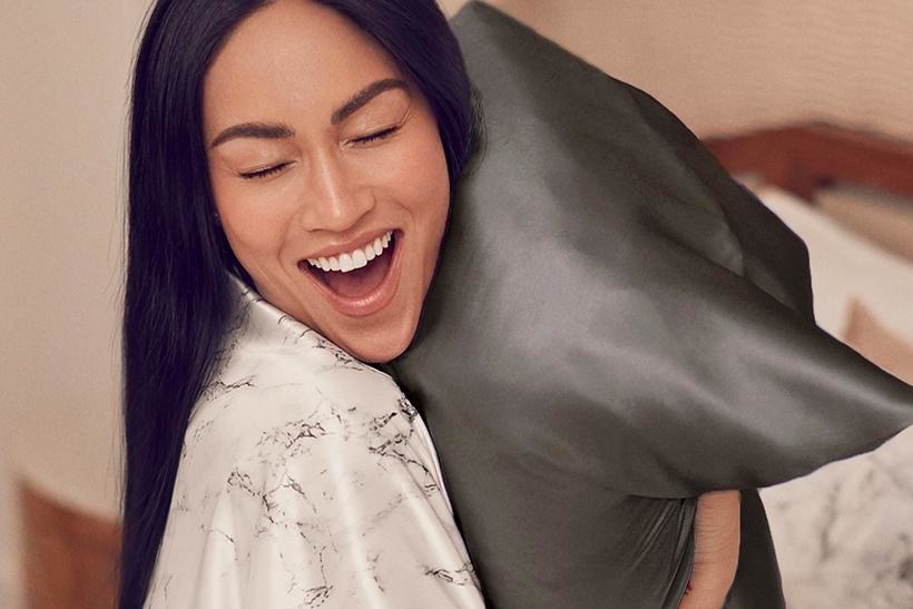 Model hugging a pillow with the silk pillowcase on it in black