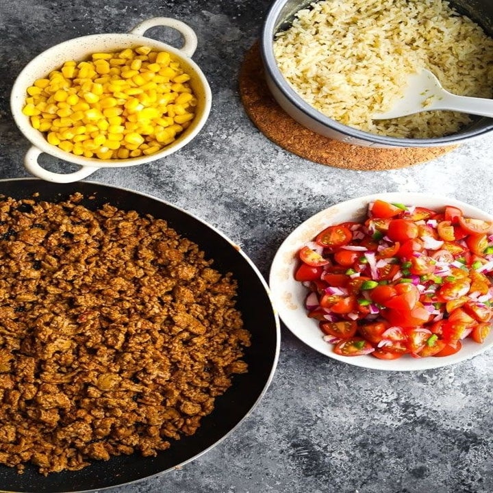 Cooked turkey meat in a skillet alongside bowls of corn, rice, and salsa.