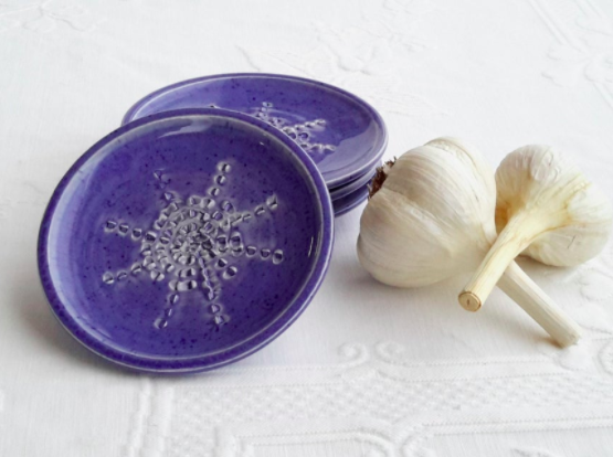 A circular glazed ceramic grating dish next to several heads of fresh garlic