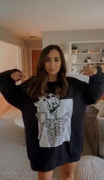 a reviewer in an oversized black sweatshirt with a white graphic of a skeleton drinking coffee