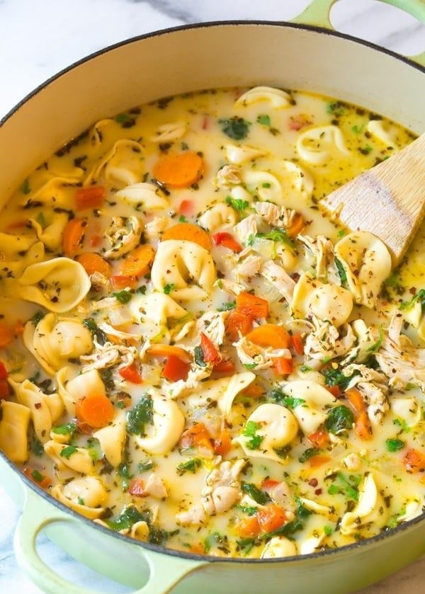 A Dutch oven filled with creamy chicken tortellini soup with carrots and fresh herbs.