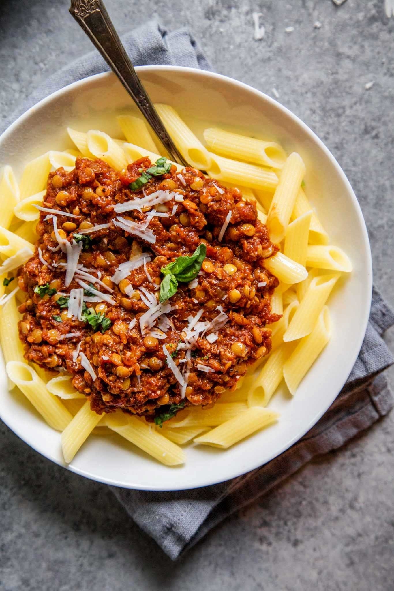 A plate of penne topped with lentil Bolognese, grated cheese, and basil.