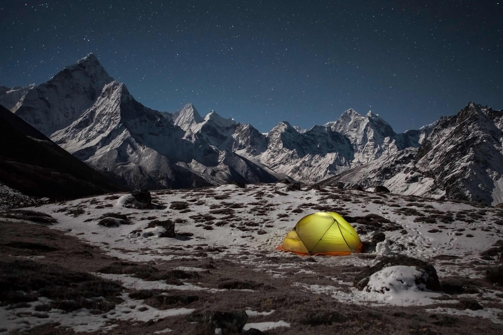 A glowing tent set up under a starry sky, surrounded by snowy mountains