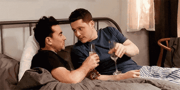 David and Patrick toast champagne and kiss in bed