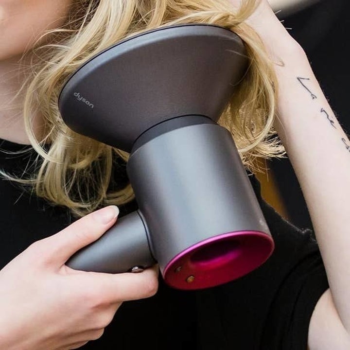 Model holding the hair dryer with diffuser attachment  up to their hair
