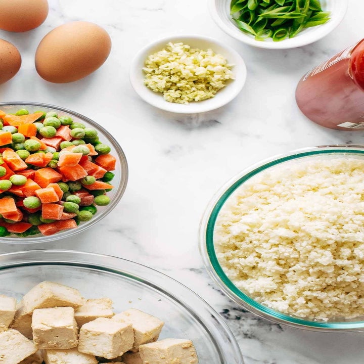 Cauliflower rice, frozen peas and carrots, chopped tofu, and eggs on a counter top.