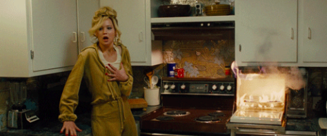 Jennifer Lawrence holding her chest and looking shocked while a microwave is on fire. 