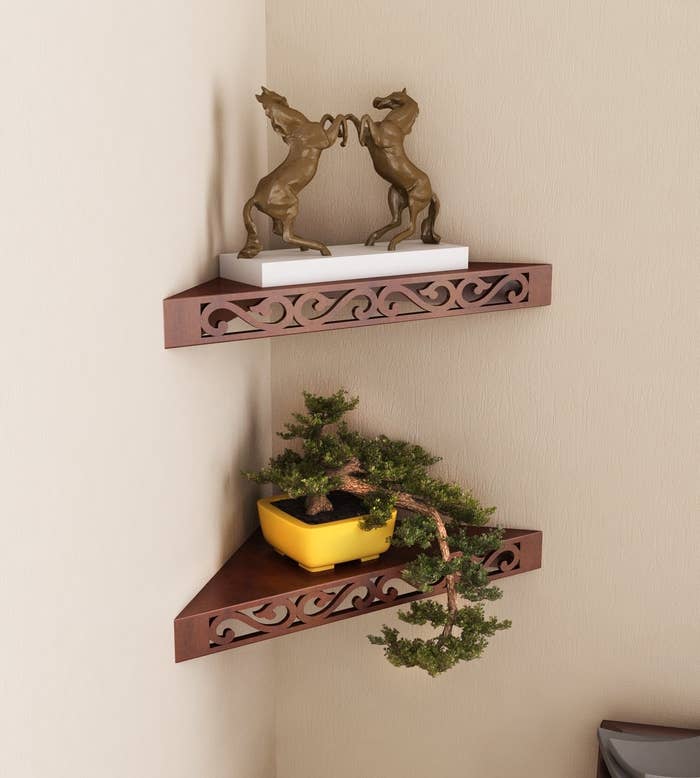 The corner shelf with detailing on the front panel, pictured with a plant and a showpiece.