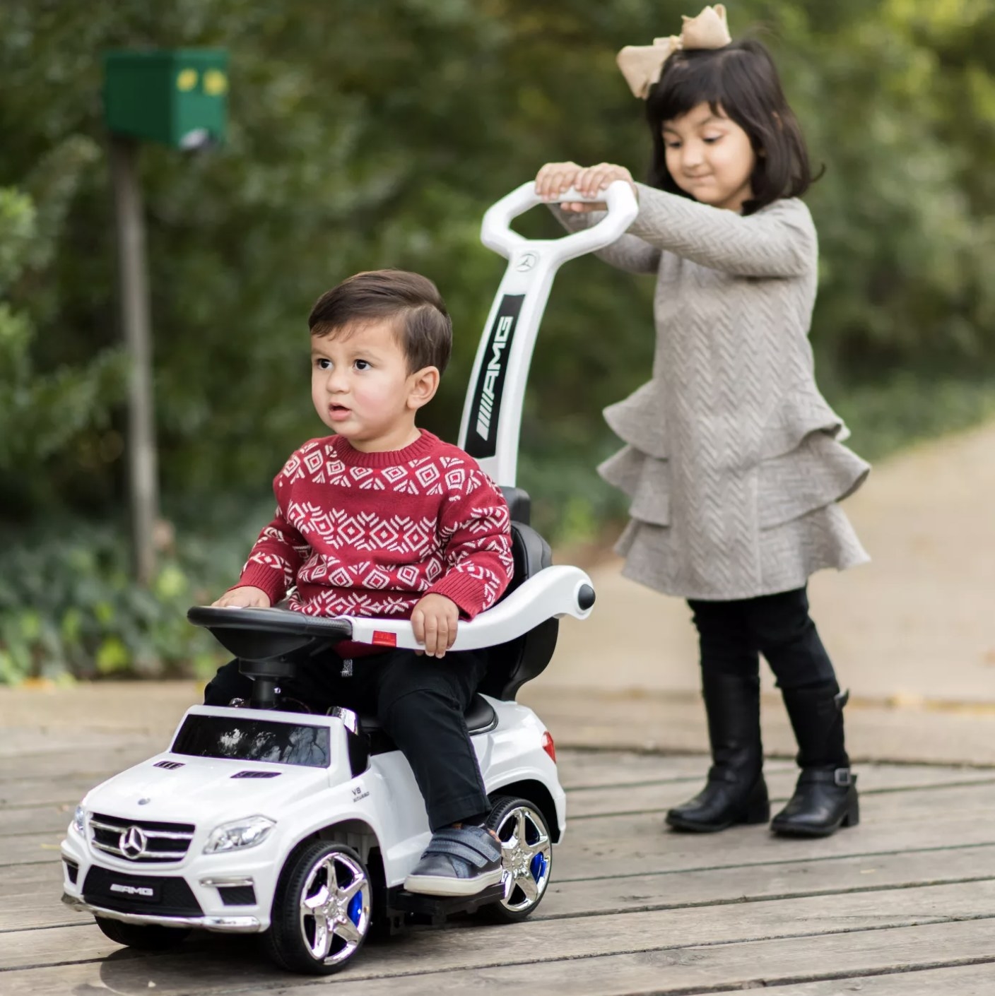 A child pushing another child on a push stroller shaped like a white car