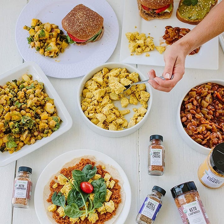 Two hands reaching for serving dishes of various meats and veggies, surrounded by bottles of spices