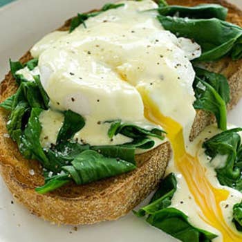 A cooked poached egg split in half with egg running out of the middle, placed on top of a piece of toast and spinach
