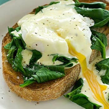 A cooked poached egg split in half with egg running out of the middle, placed on top of a piece of toast and spinach