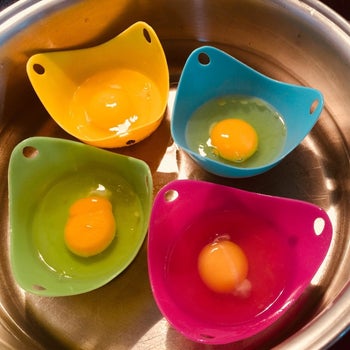 A set of four silicone egg poaching cups with raw egg inside sitting in a pot of water