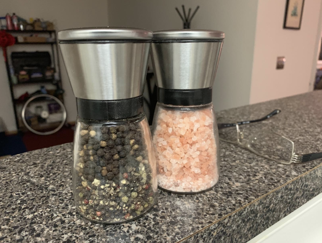 Two glass grinders with stainless steel tops full of pepper and sea salt