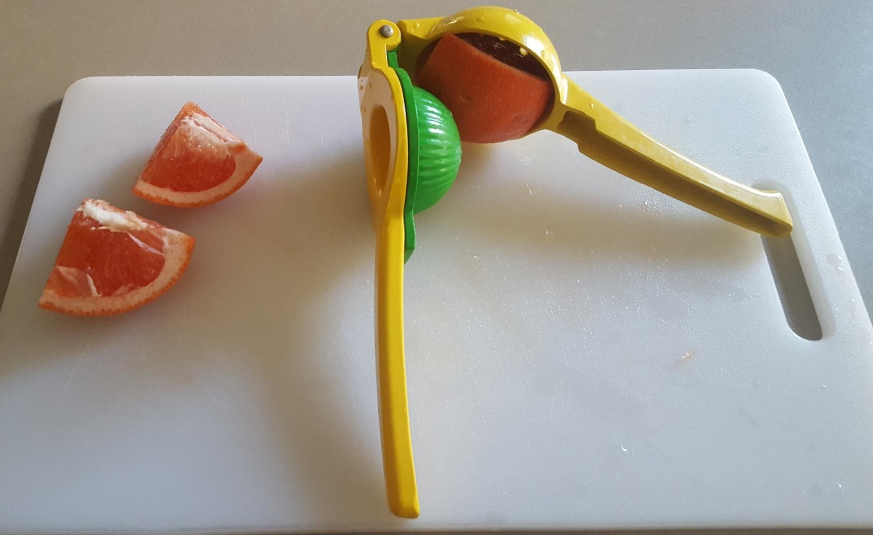 A yellow and green citrus juicer with a slice of orange inside, placed next to two slices of orange on a cutting board