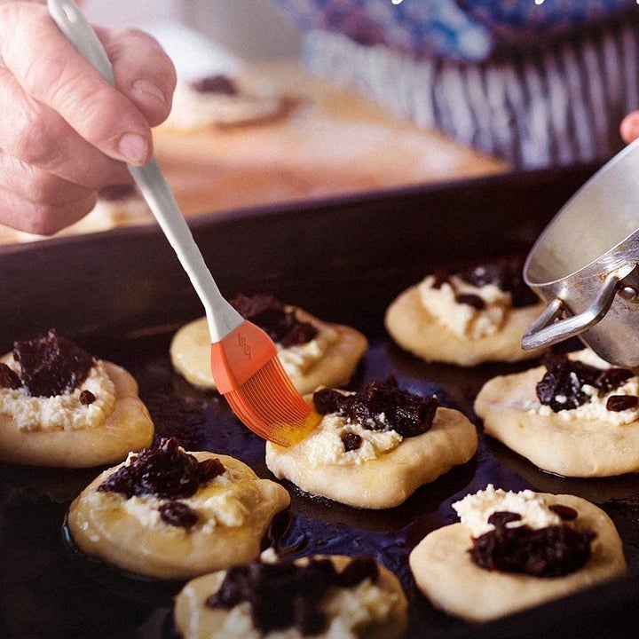 A small orange silicone basting brush applying glaze to a tray of pastries