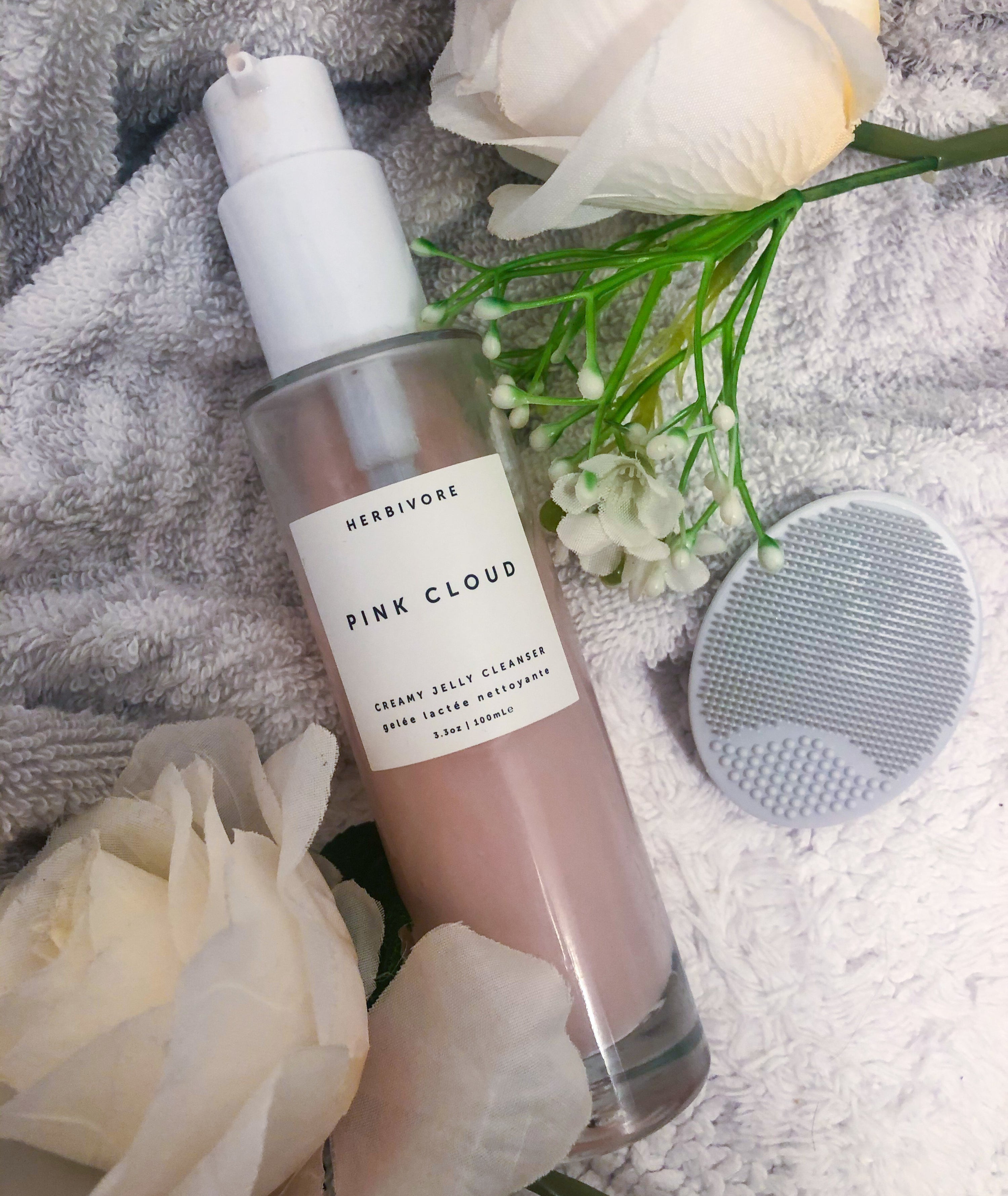 A flatlay of the facial cleanser surrounded by flowers, textiles and facial scrubbers