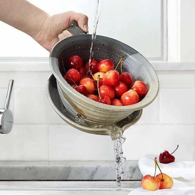 Hand tilting the strainer into the sink to drain water out as cherries sit inside the deep bowl