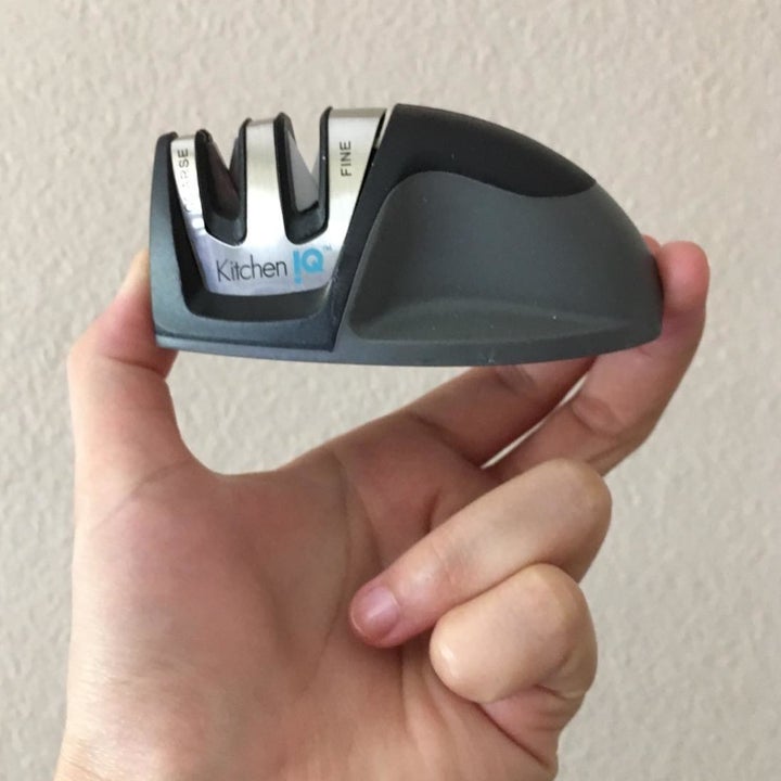 Hand holding a knife sharpener with two slots against a white background.
