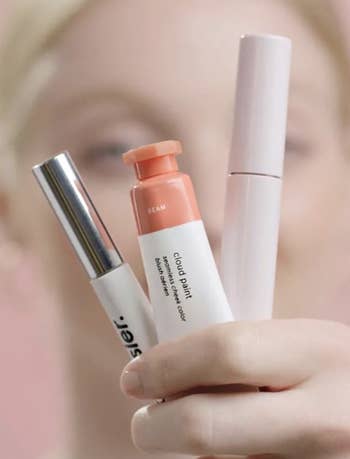 a model holding a tube of peach cloud paint, mascara, and boy brow
