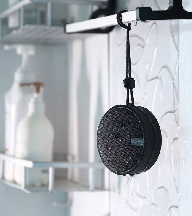 A wet INSMY bluetooth speaker hanging from a bathroom shelf
