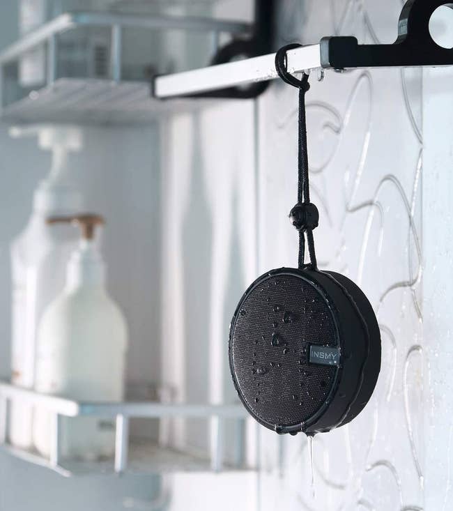 A wet INSMY bluetooth speaker hanging from a bathroom shelf