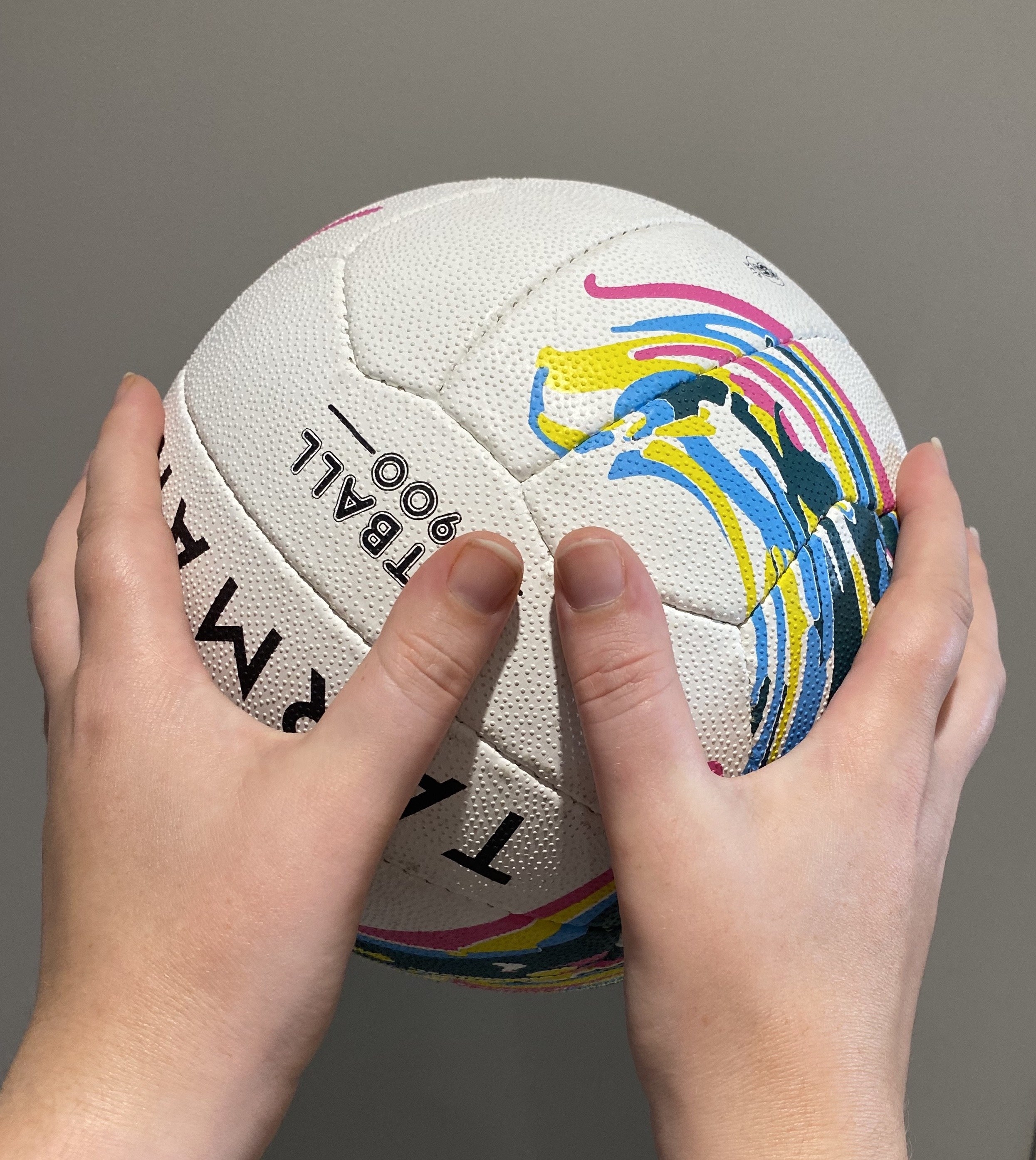 Hands holding a netball with the thumbs close to each other and the fingers splayed around the ball