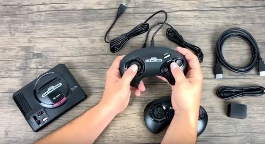Hand holding one of he controllers and showing the console and accessories