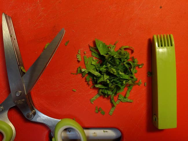 Reviewer's scissors and a pile of cilantro cut using them, plus the cover with the cleaning comb built in
