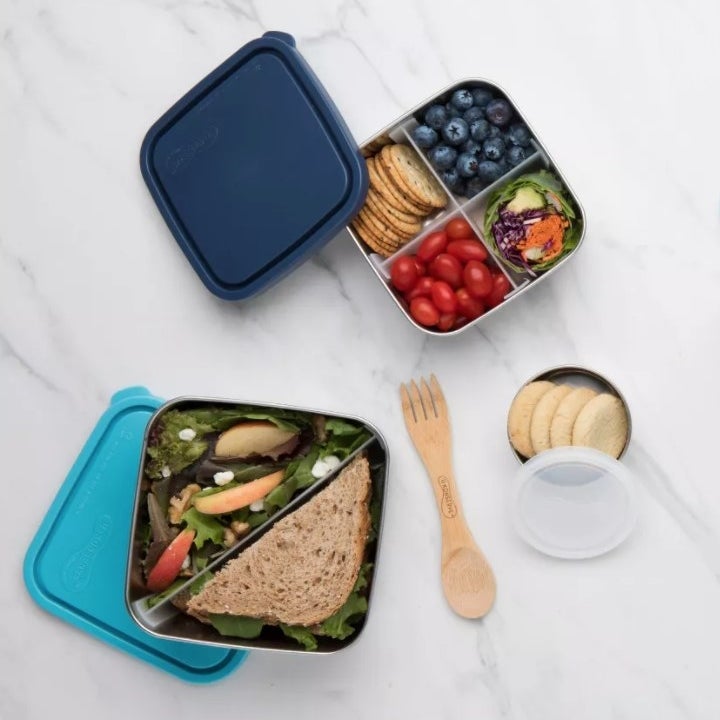 Three square stainless steel lunch container, two of them with a diagonal plastic divider and one with plastic dividers creating four smaller compartments
