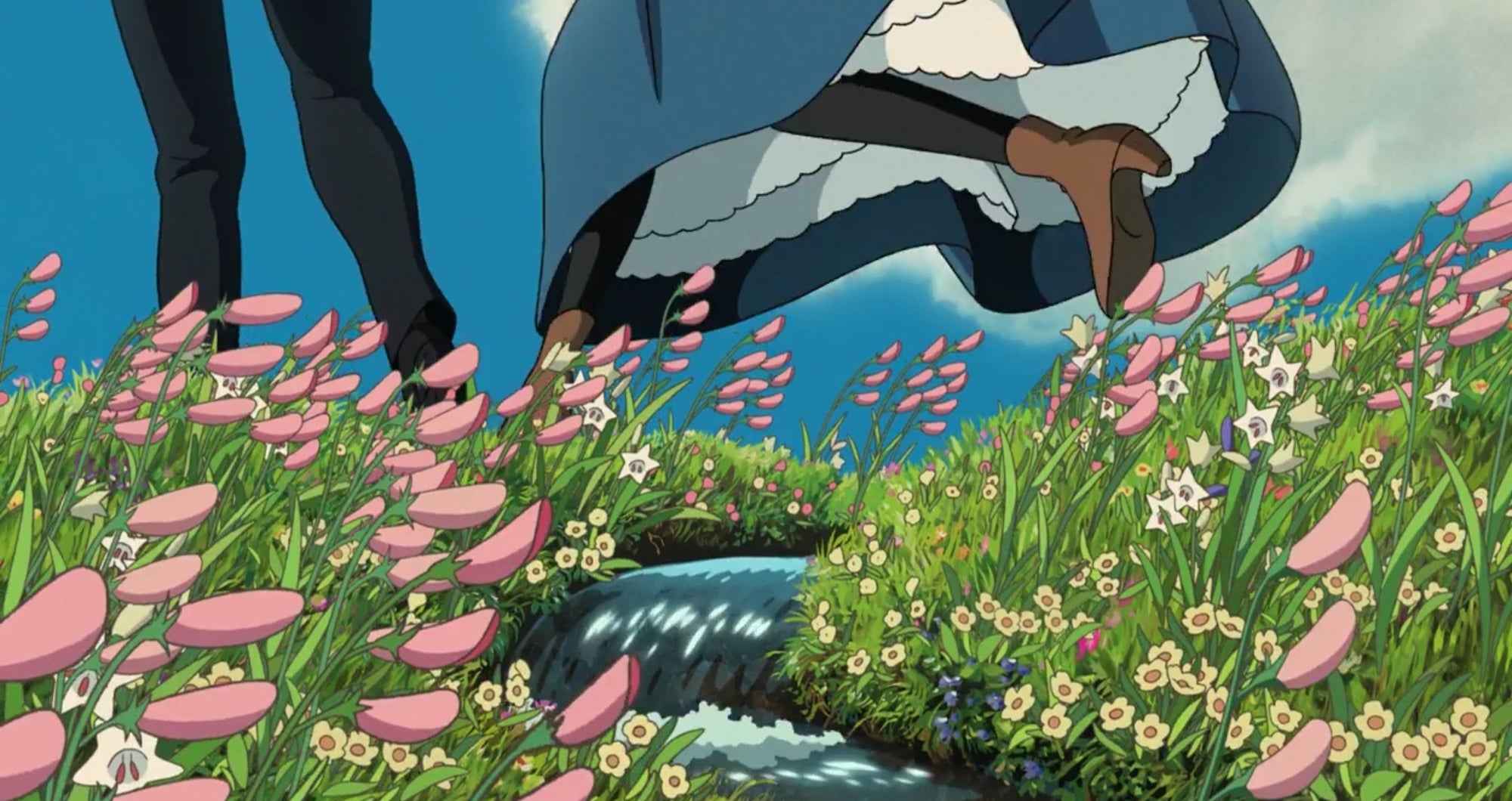 Two sets of feet jump over a small stream in the middle of a field of flowers