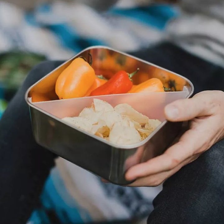 A person holding the square stainless steel lunch container with a diagonal plastic divider