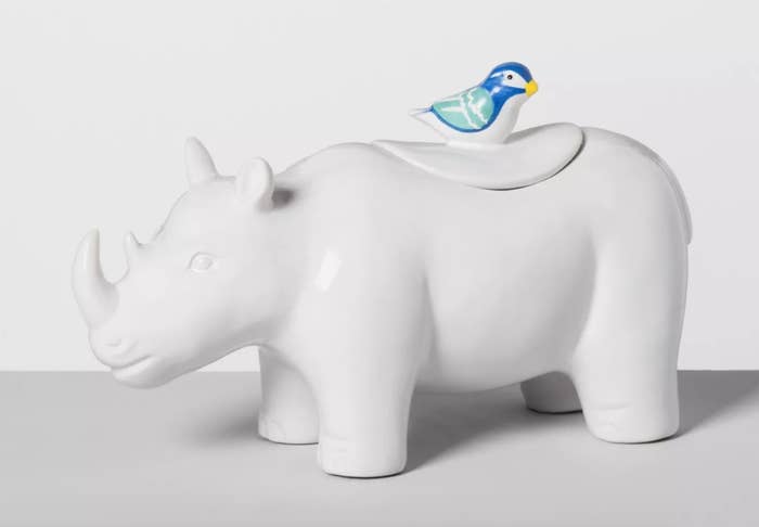 A white cermaic rhino cookie jar with a blue bird on its back, as the handle to open the top