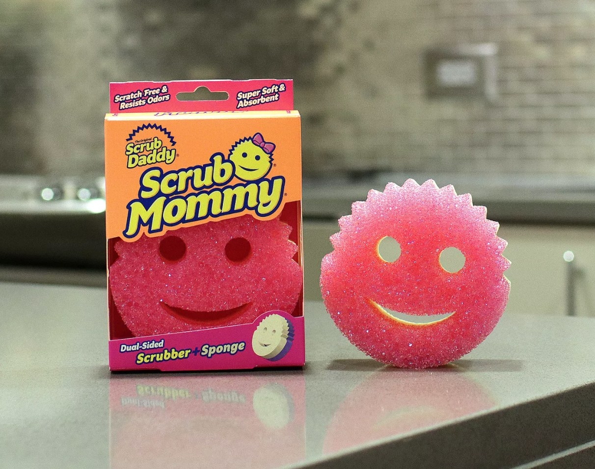 A sponge with pink scrub surface on one side and yellow sponge on the other side, with smiley face cutouts