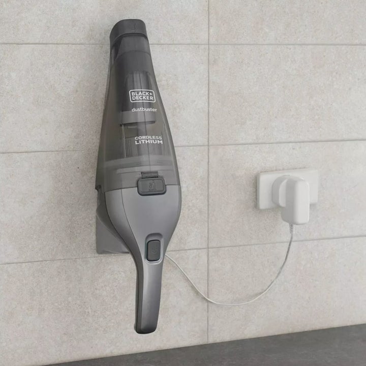 A gray handheld vacuum plugged into a wall outlet and holder