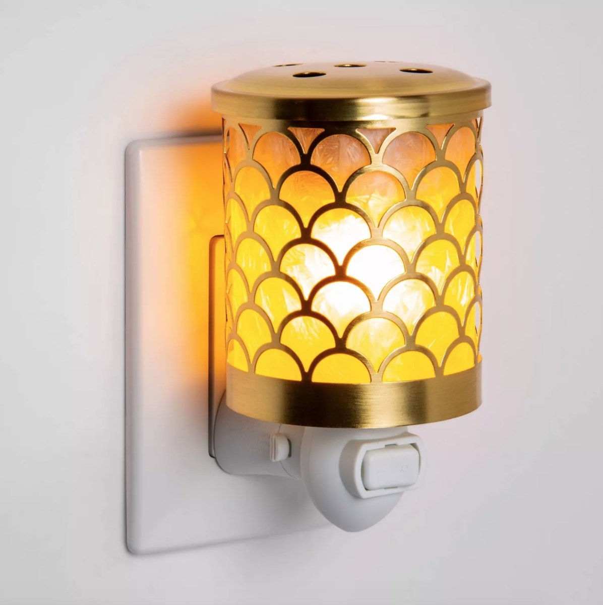 A gold wax warmer that plugs into the outlet with a warm yellow glow