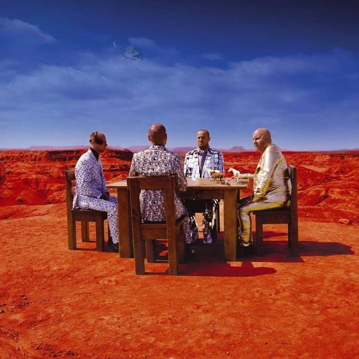 Four men dressed in patterned suits sitting at a dining table in the desert