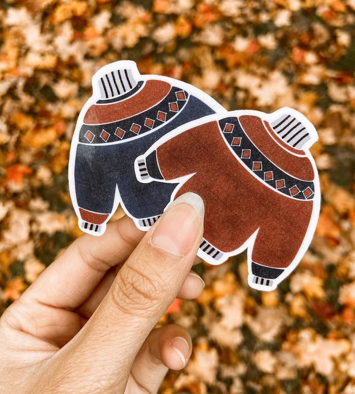 A person holding two sweater stickers