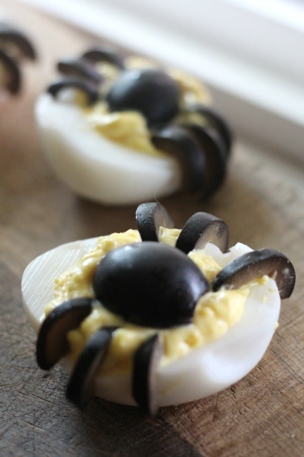 Two deviled eggs topped with sliced olives in the shape of spider.