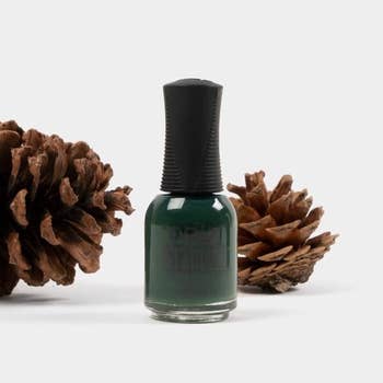 a bottle of dark green nail polish next to pinecones