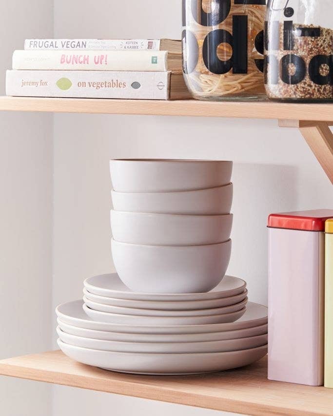 Gray stoneware plates and bowls stacked in a single pile on a wooden shelf