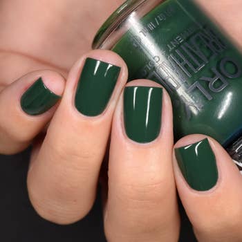 a model wearing the green nail polish while holding the polish bottle