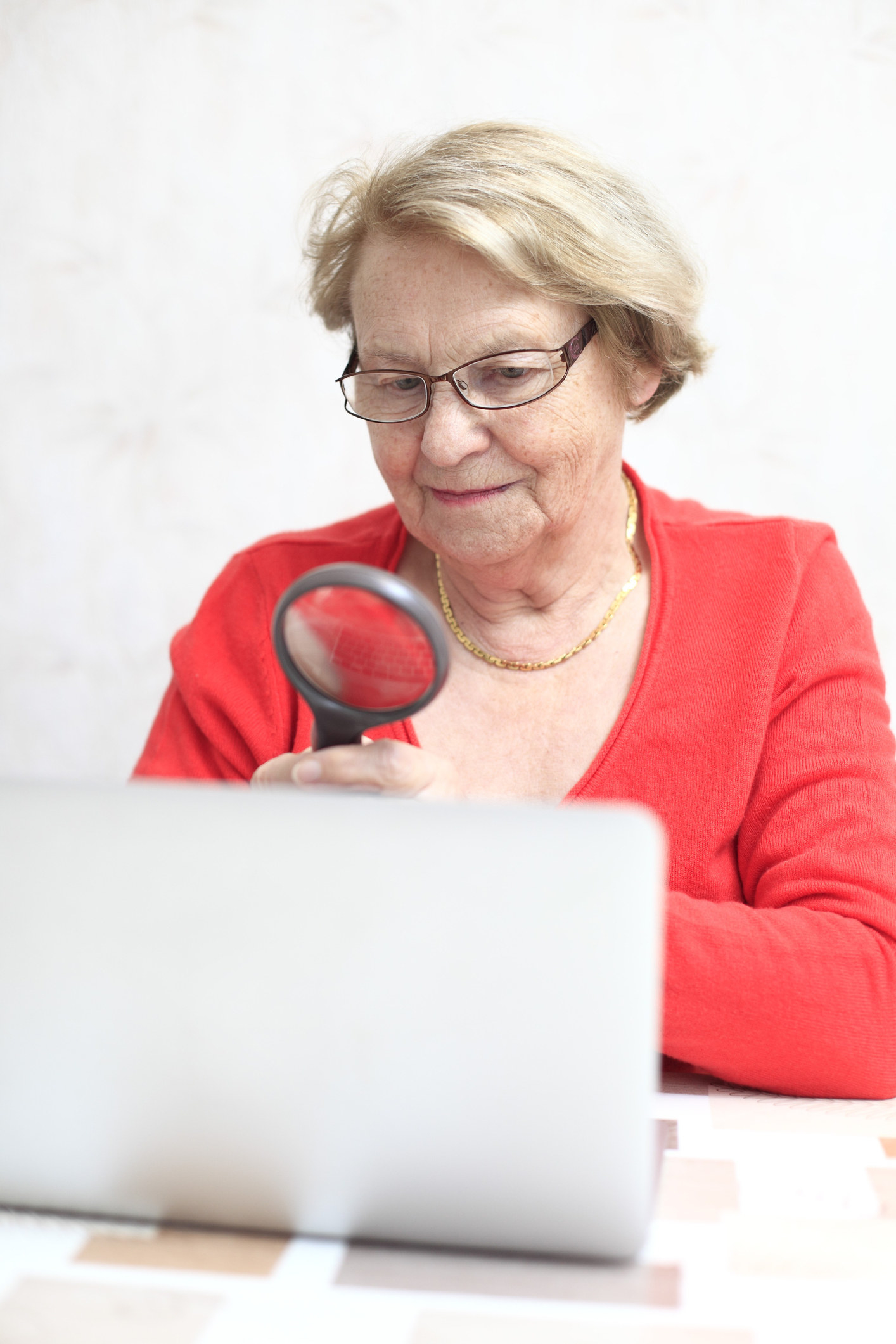 elderly woman with a magnifying glass looking at a laptop